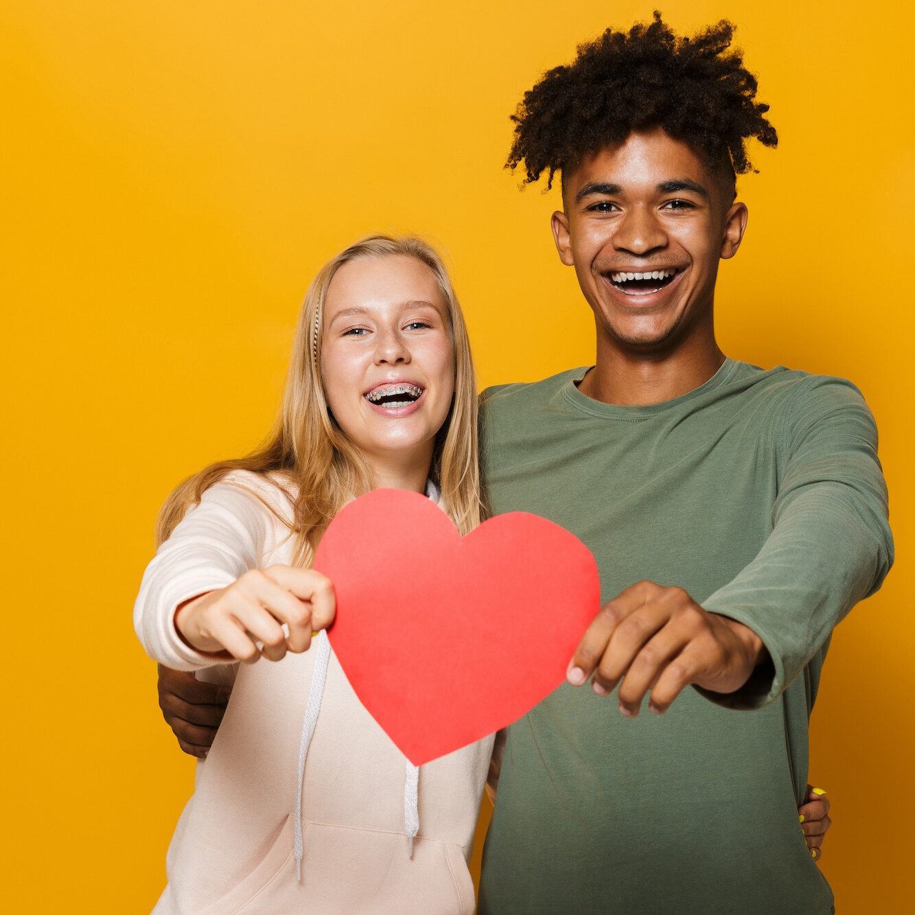 Photo of teenage friends man and woman 16-18 holding paper heart isolated over yellow background